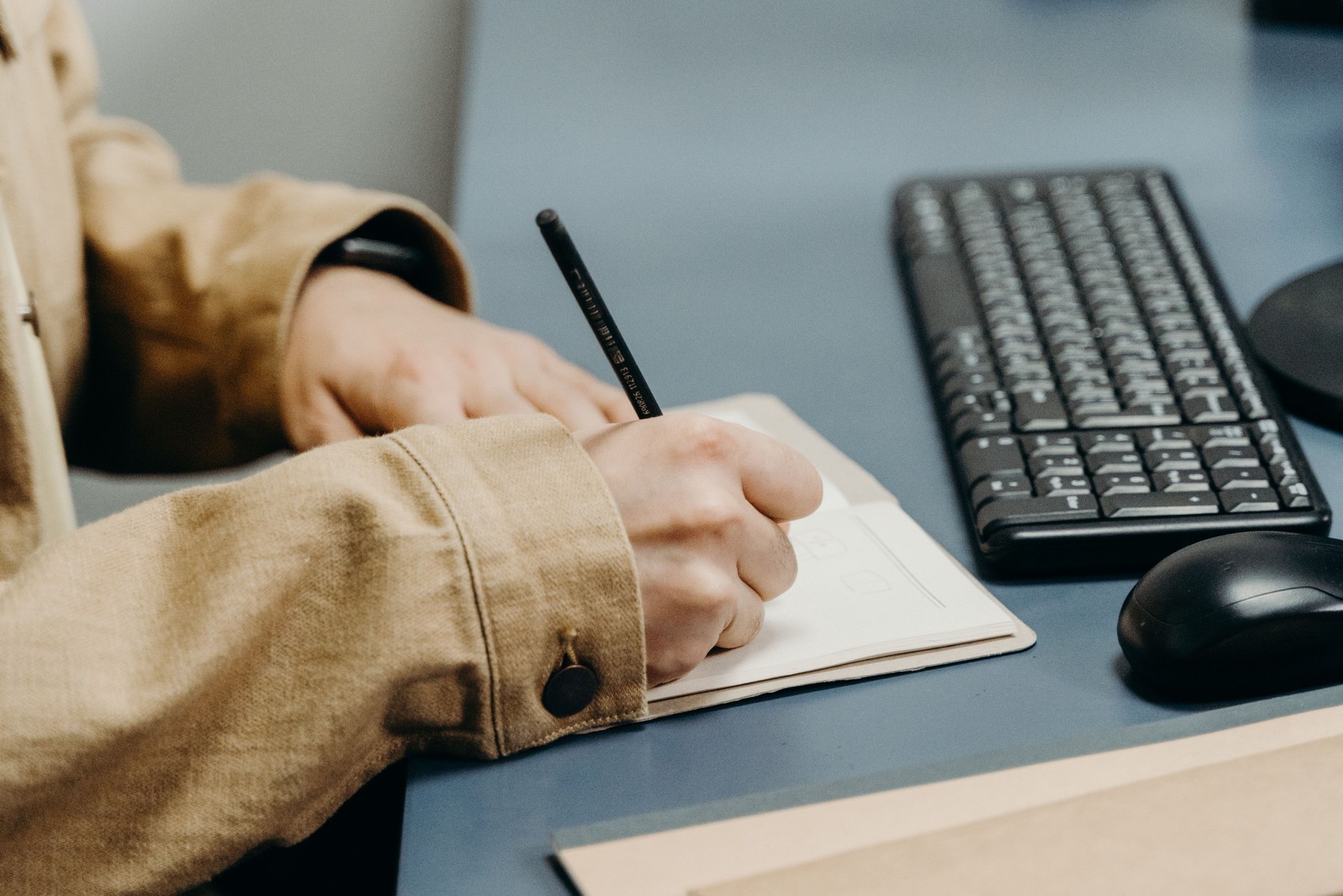 Close up of a person's hands writing in a notebook on an office desk, representing the shift from planning content to writing real cold email copy