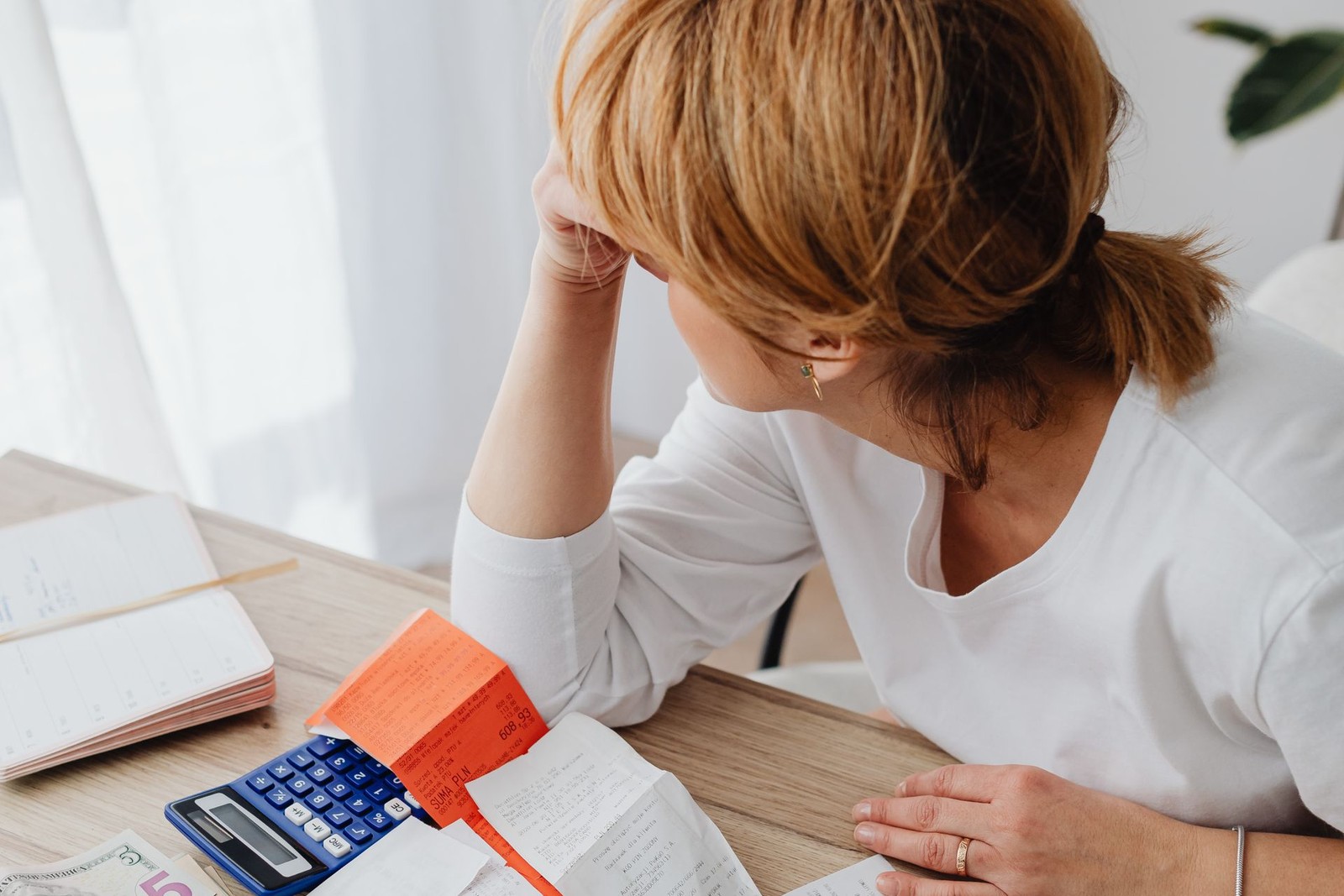 A woman surrounded by receipts, a calculator, and cash, overwhelmed while reviewing her small business expenses