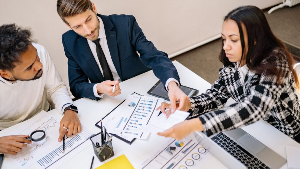 Three people in a corporate style meeting, reviewing printed charts and documents at a table