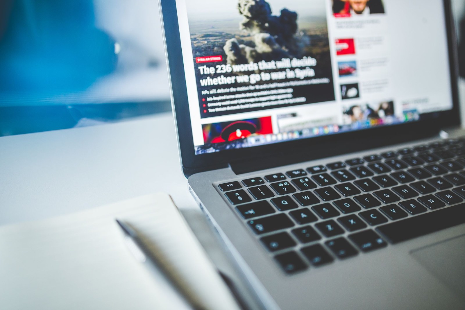 A laptop open to a news article, with a notebook and pen beside it