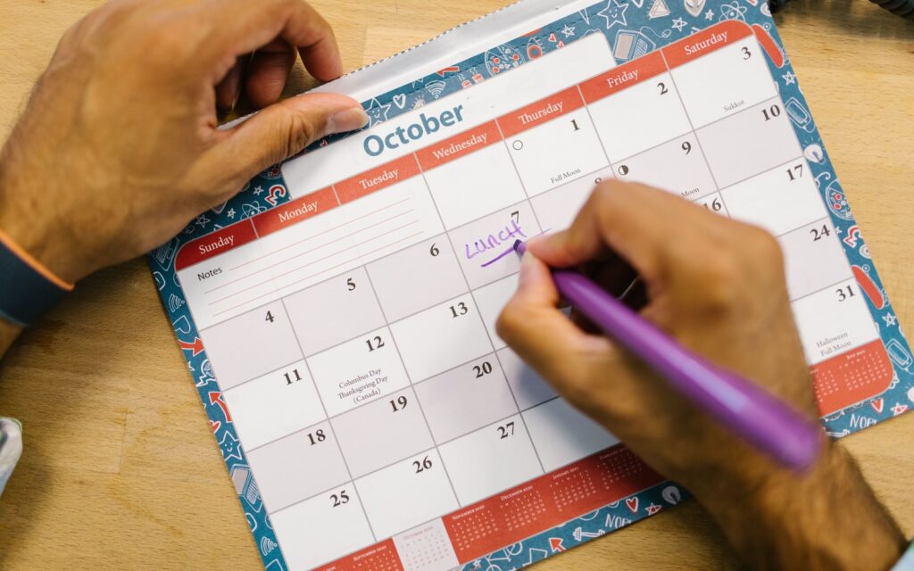 A hand writing a time block into a paper desk calendar