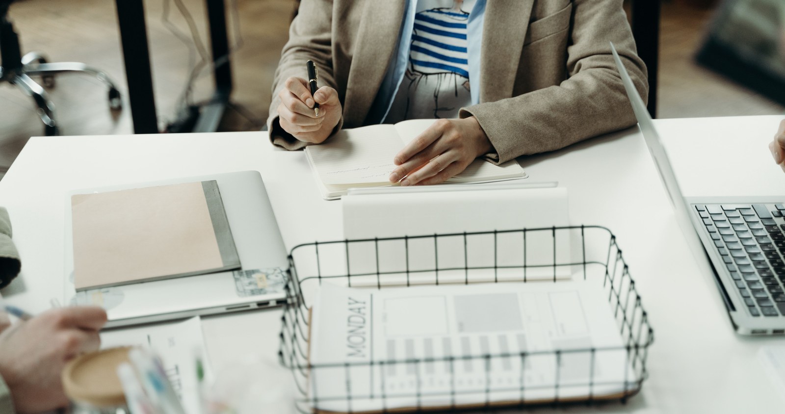 A person writing in a Monday planner next to an open laptop on a desk