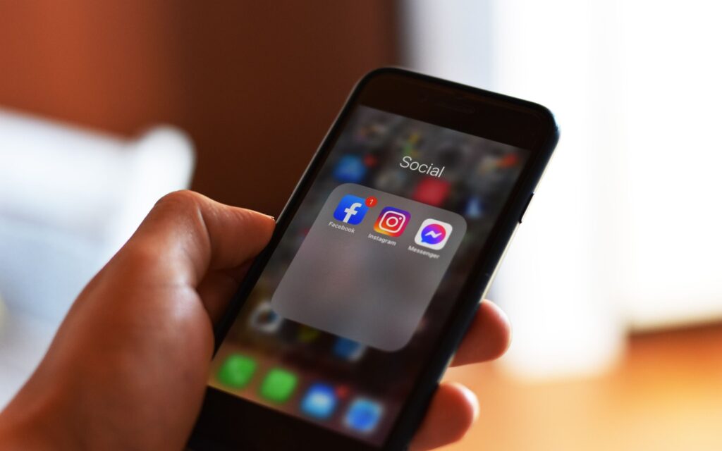 A hand holding a phone open to a folder of social media apps