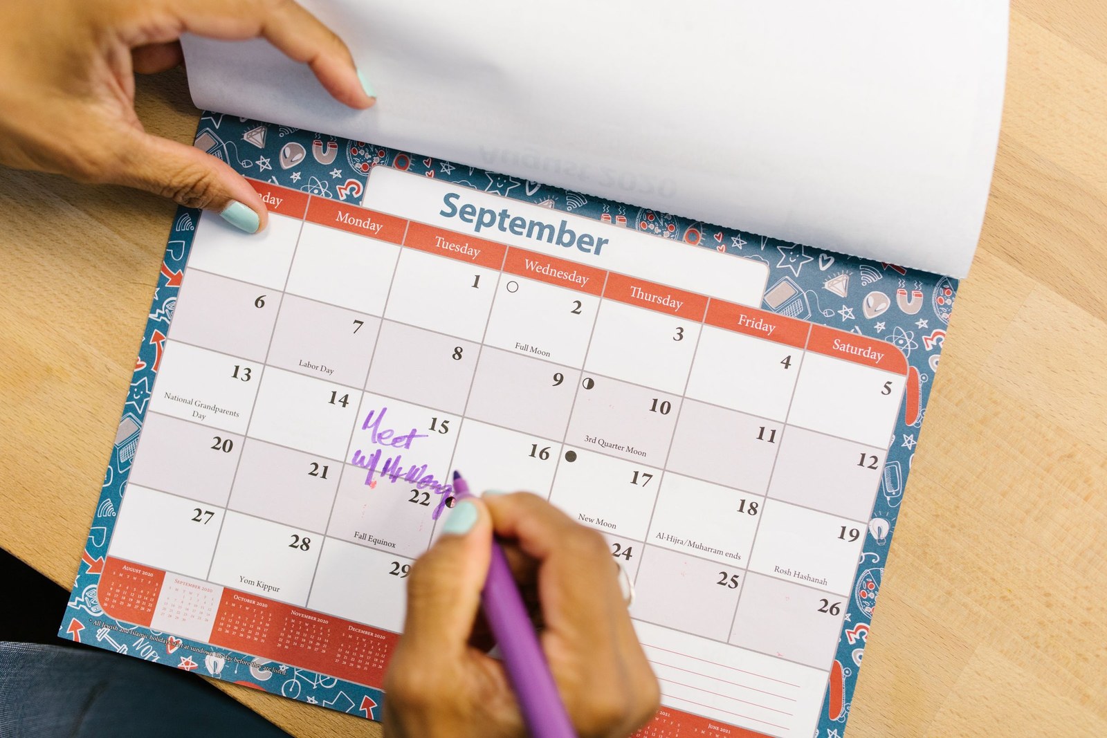 A hand writing a plan into a paper monthly calendar