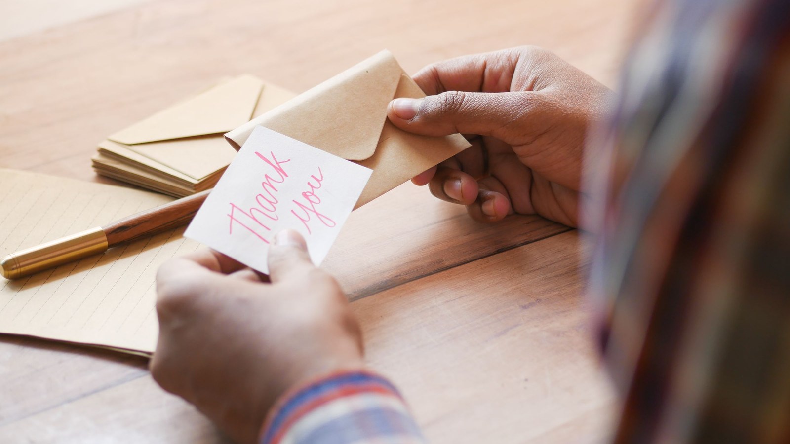 Hands holding a small handwritten thank you note beside envelopes