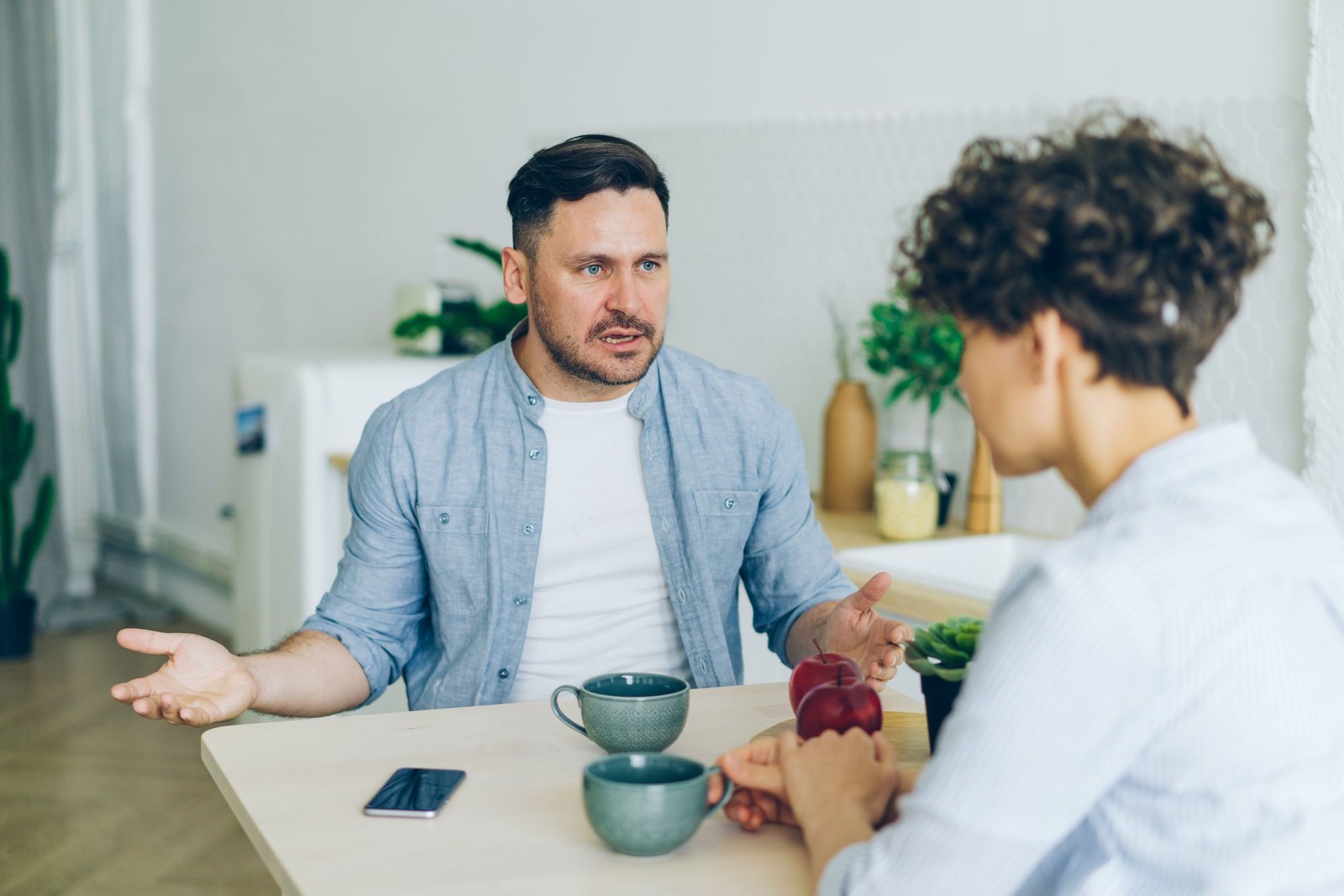 2 people talking openly across a table with cups and a phone between them